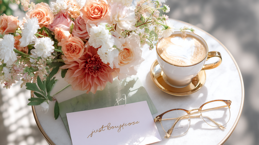 Flat lay of a luxury flower bouquet with coral roses, pink dahlias, and white lisianthus on a Walnut Creek café table next to a cappuccino and handwritten card, sunlight filtering through nearby trees.