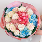 Top-down view of pastel flower arrangement featuring pink, blue, and ivory hydrangeas and roses in lush pink wrap.