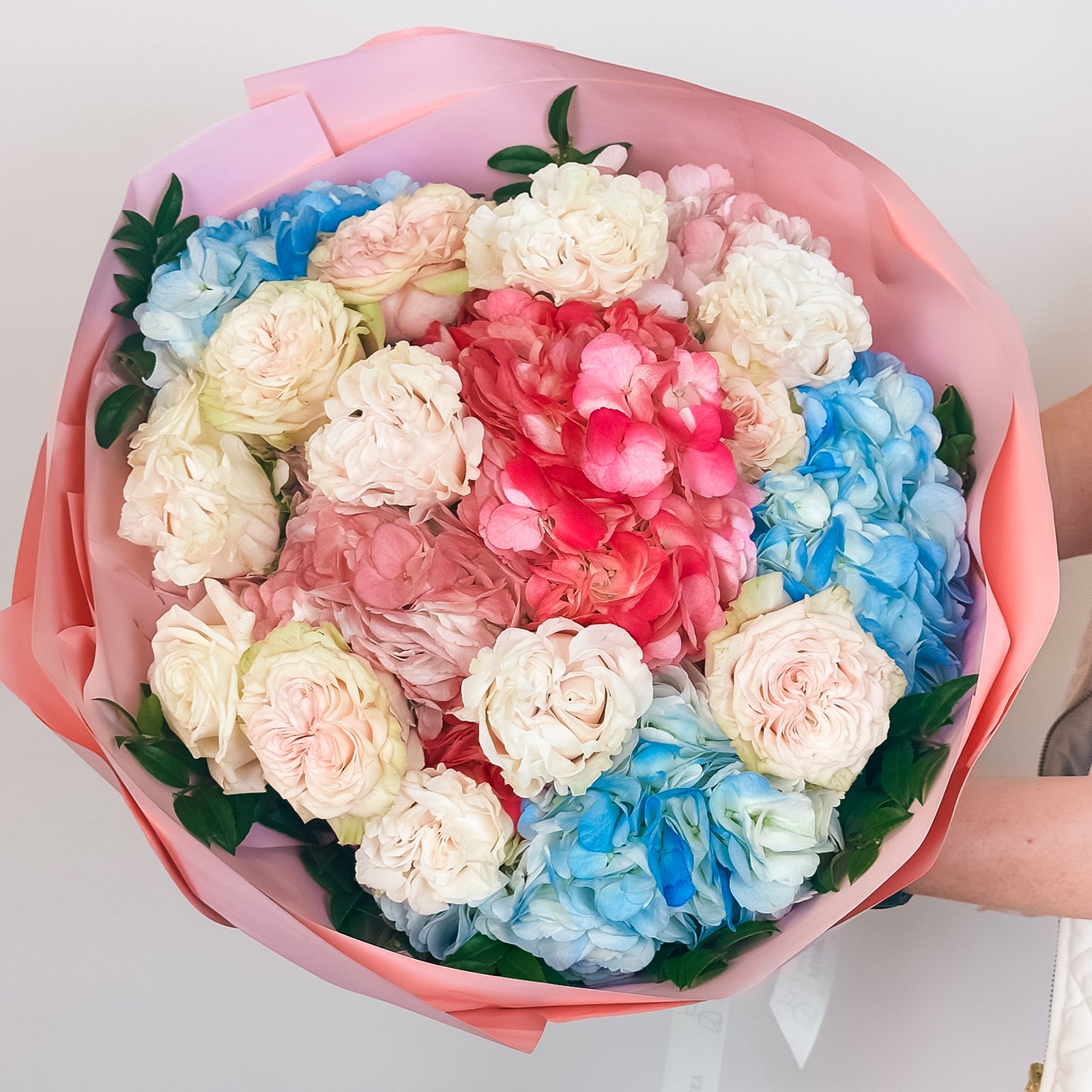 Top-down view of pastel flower arrangement featuring pink, blue, and ivory hydrangeas and roses in lush pink wrap.
