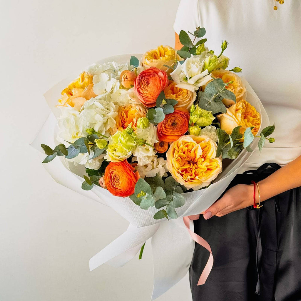 Spring Colors bouquet with orange ranunculus and yellow roses wrapped in white paper