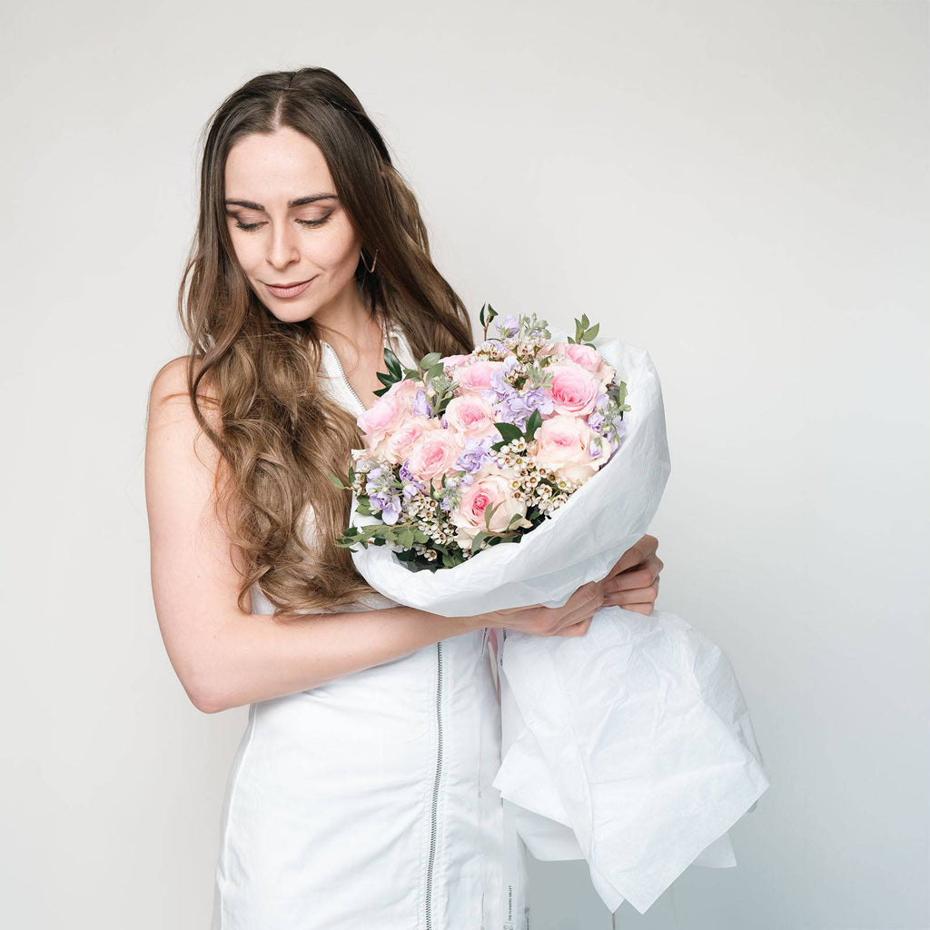 Wrapped bouquet of pastel blooms resting on a table—featuring roses, matthiola, and waxflower.