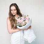 Wrapped bouquet of pastel blooms resting on a table—featuring roses, matthiola, and waxflower.