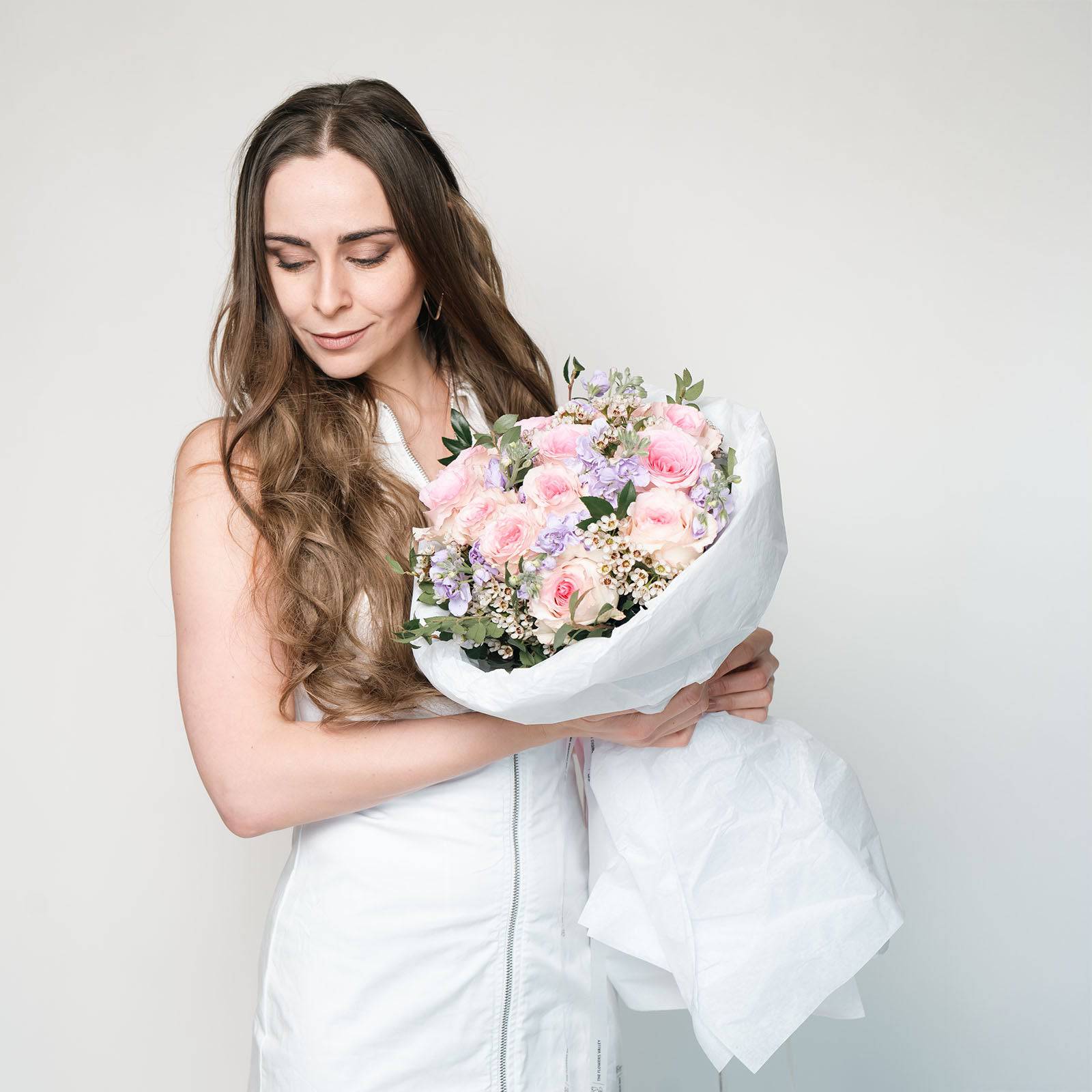 Wrapped bouquet of pastel blooms resting on a table—featuring roses, matthiola, and waxflower.