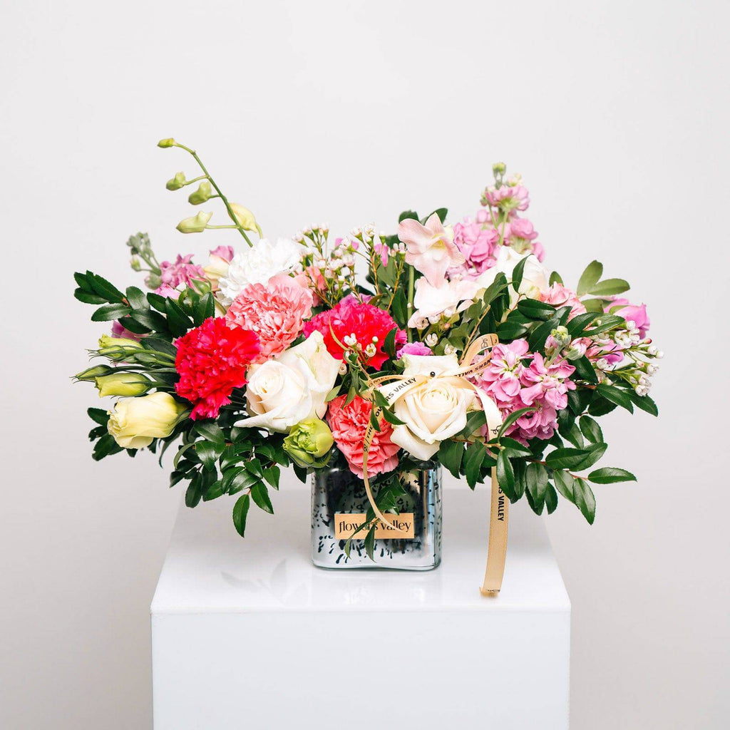 Colorful flower arrangement with pink and white blooms in a white vase, styled on a pedestal