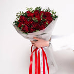 Classic bouquet of deep red roses with greenery in white wrap and red-striped ribbon—held in hand.