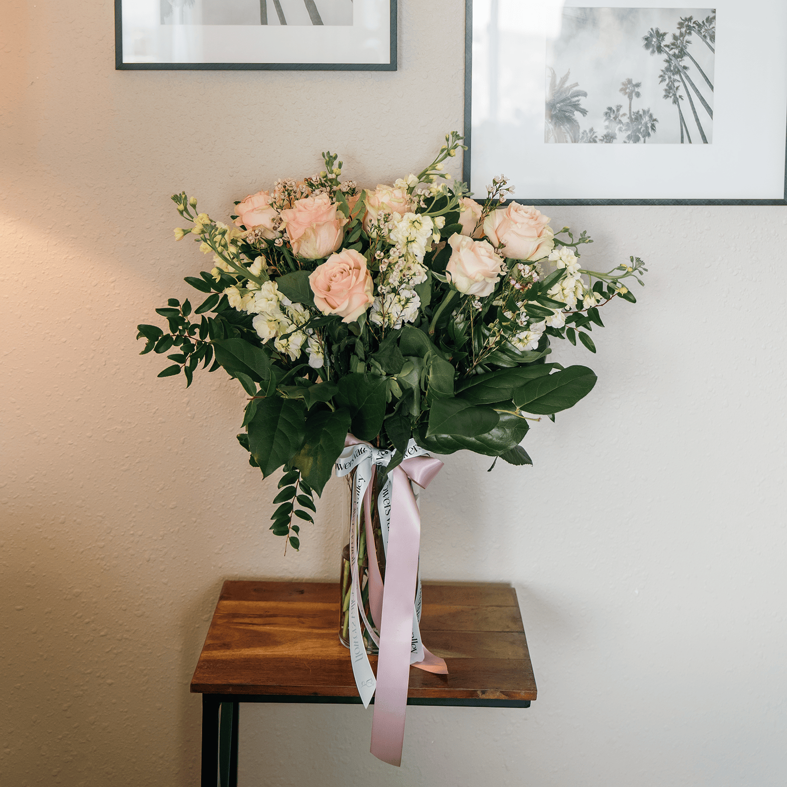 Blush flower arrangement in tall glass vase placed on a wooden table