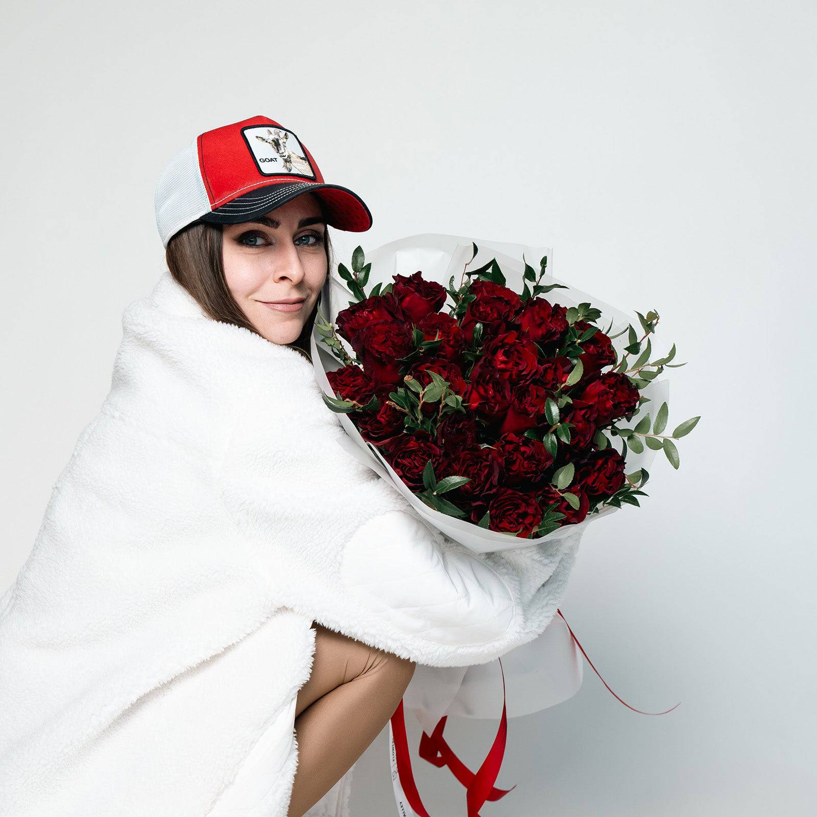 Smiling person in white holding a full red rose bouquet wrapped for gift delivery.