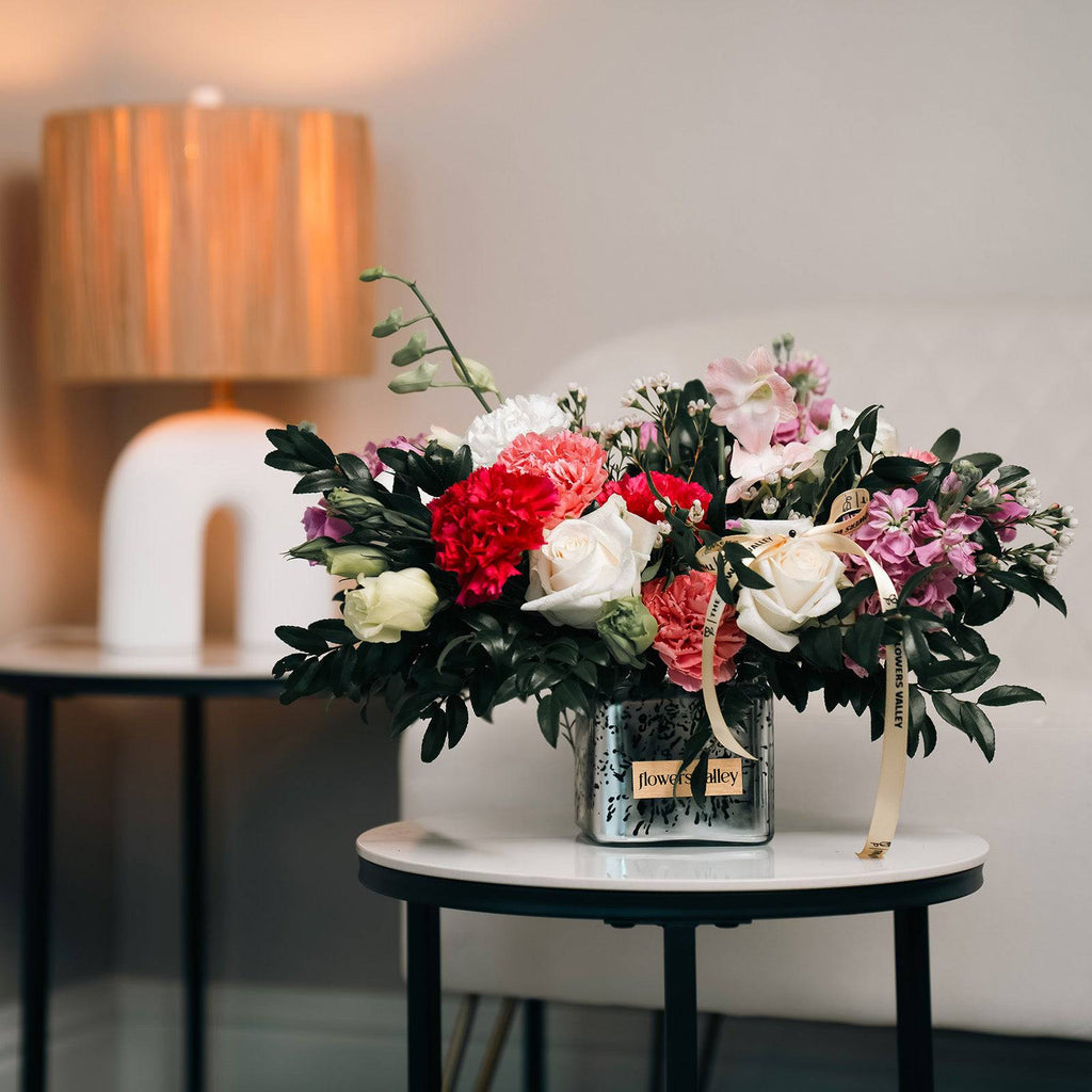 Garden Symphony flower arrangement styled on a side table next to a lamp indoors