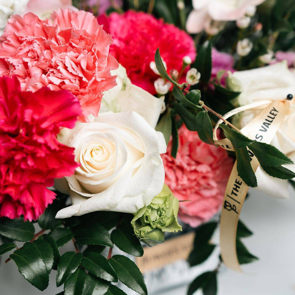 Close-up of coral carnations, white roses, and mums with greenery from the Garden Symphony bouquet