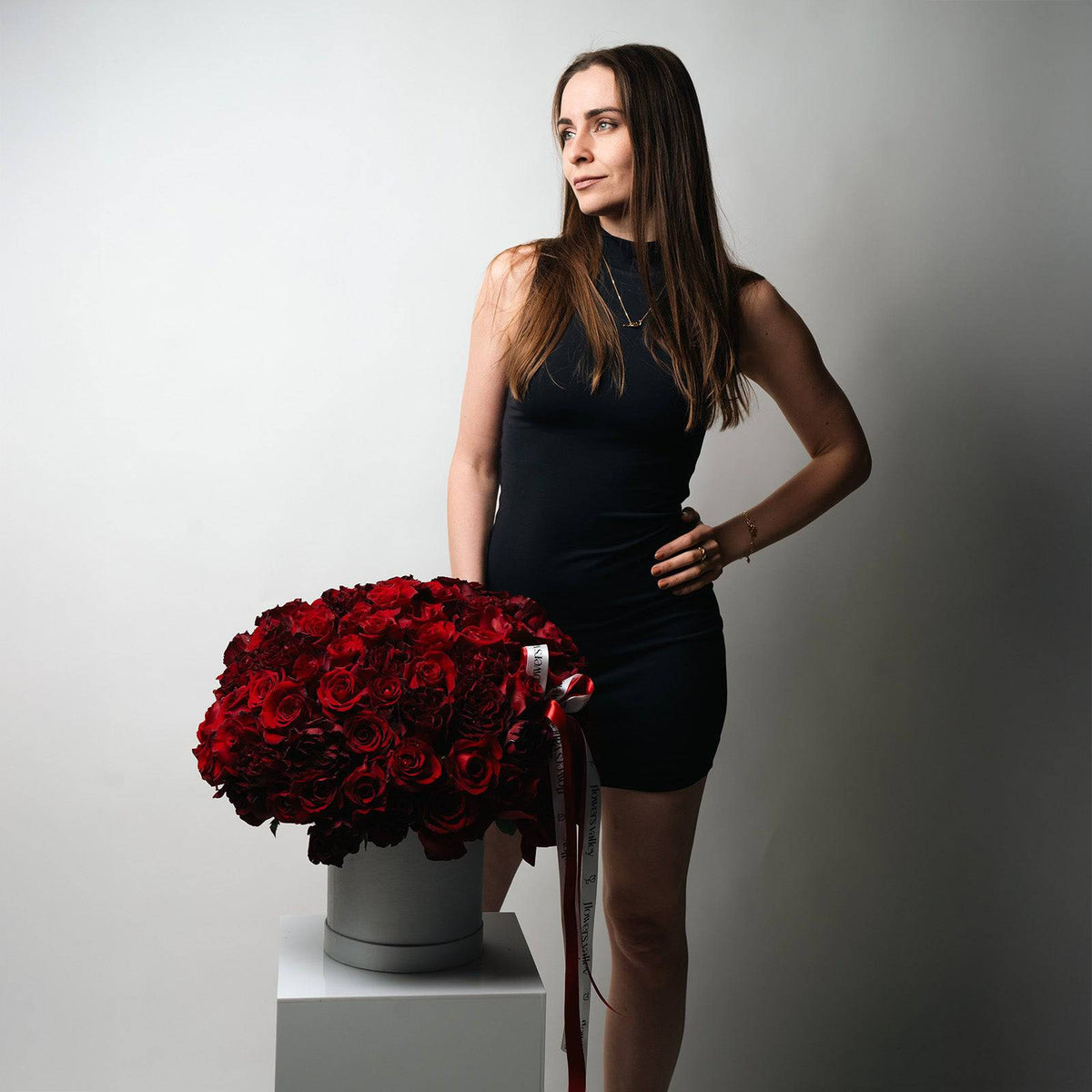 Model holding large round box of 100 red roses tied with red and white ribbon