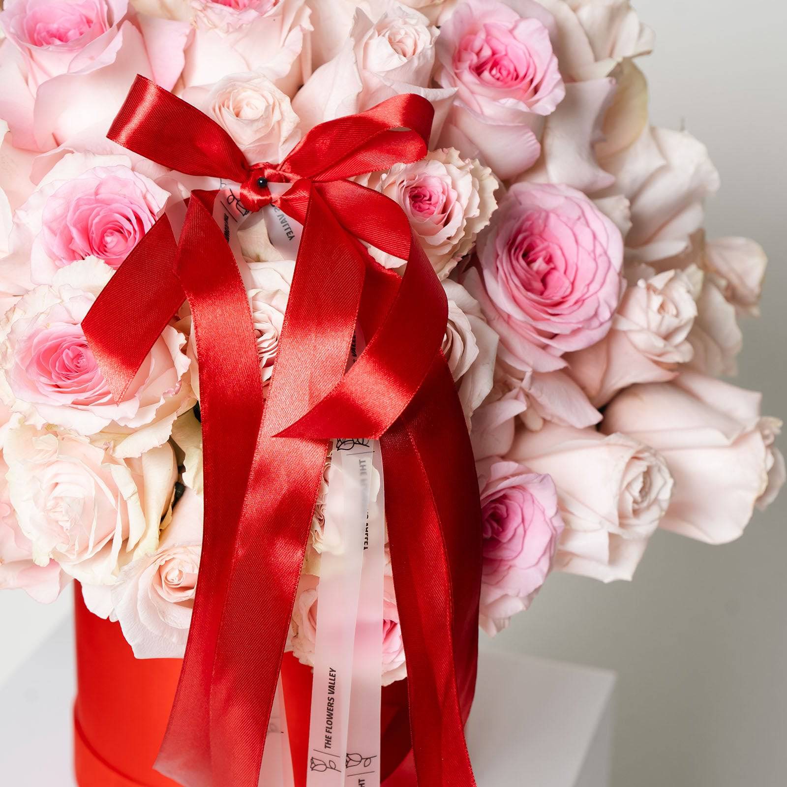 Close-up of blush rose bouquet with layered red and white ribbon detail