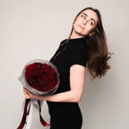 Model is holding Dozen red roses heart wrapper in a florist paper with the branded ribbons