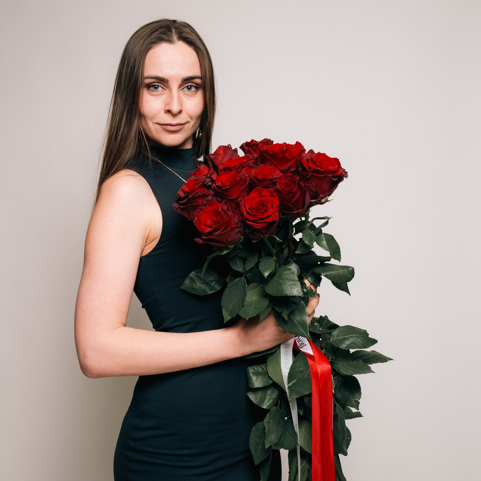 Woman holding the vibrant Dozen of Long-stem Red Roses flower bouquet in front of her, showcasing the lush red blooms, available for premium Bay Area flower delivery.