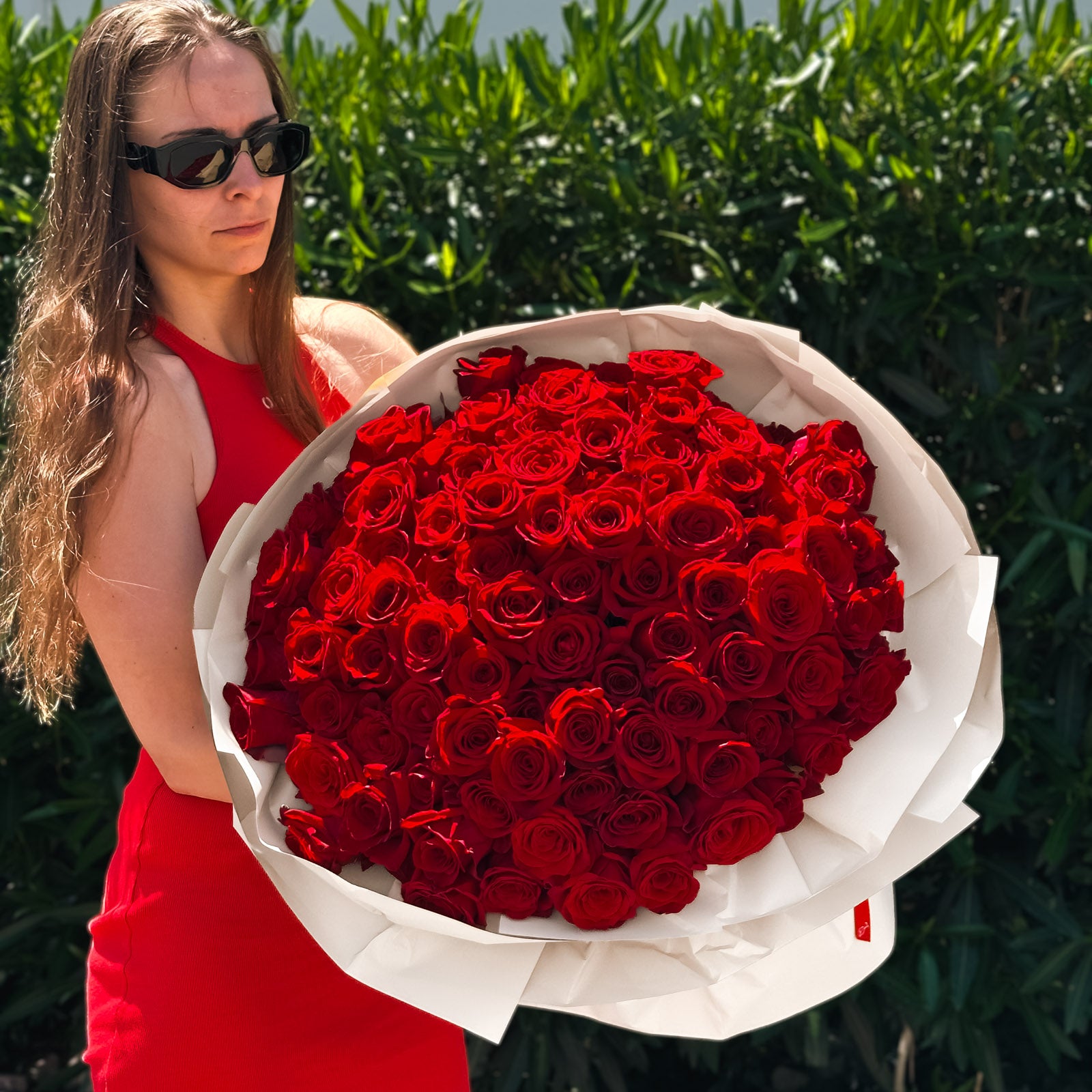 Woman in red dress holding a large, stunning Long-stem Red Roses flower bouquet, wrapped in white paper, for premium Bay Area delivery from The Flowers Valley.