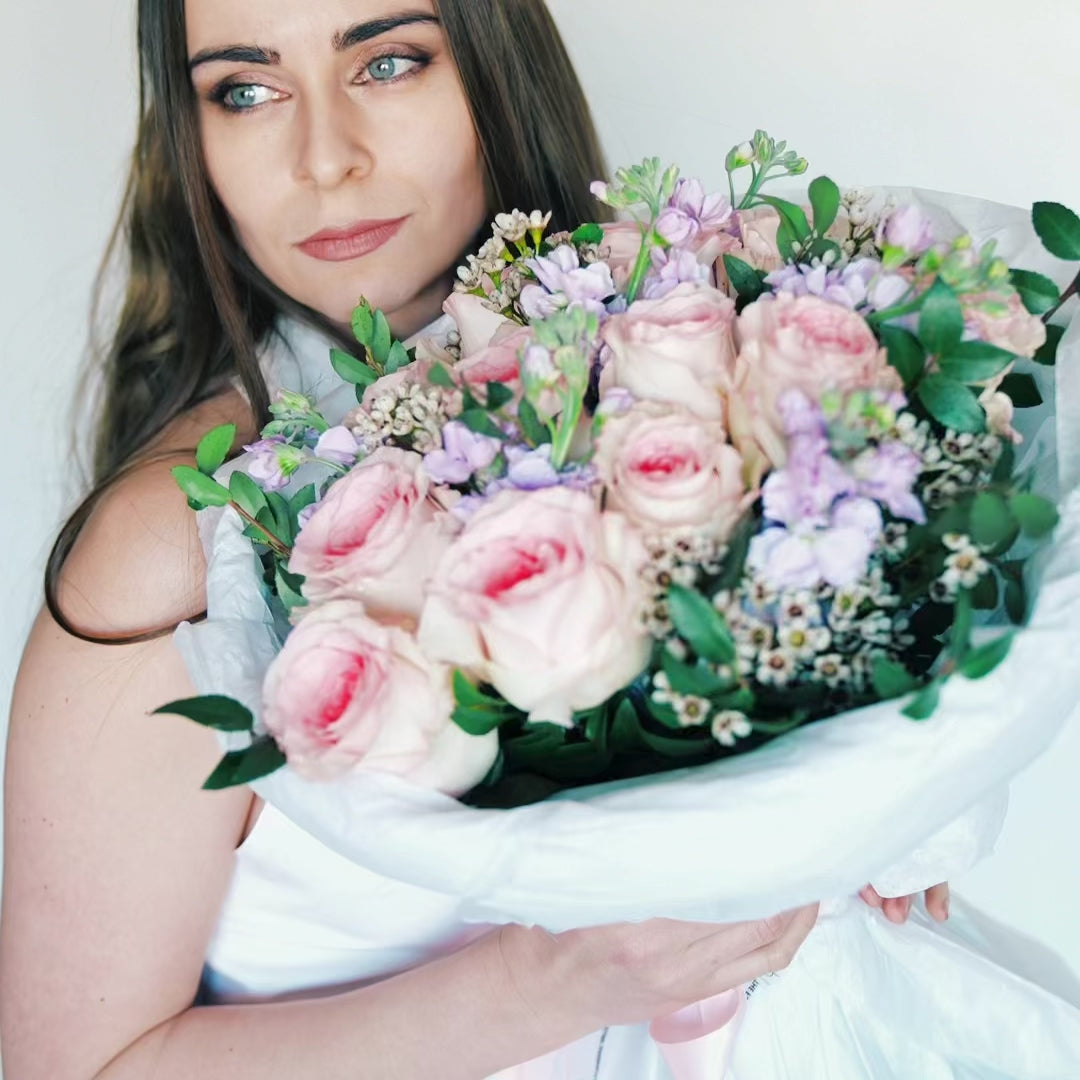 Woman in white dress holding a romantic bouquet of pink roses and lilac matthiola.