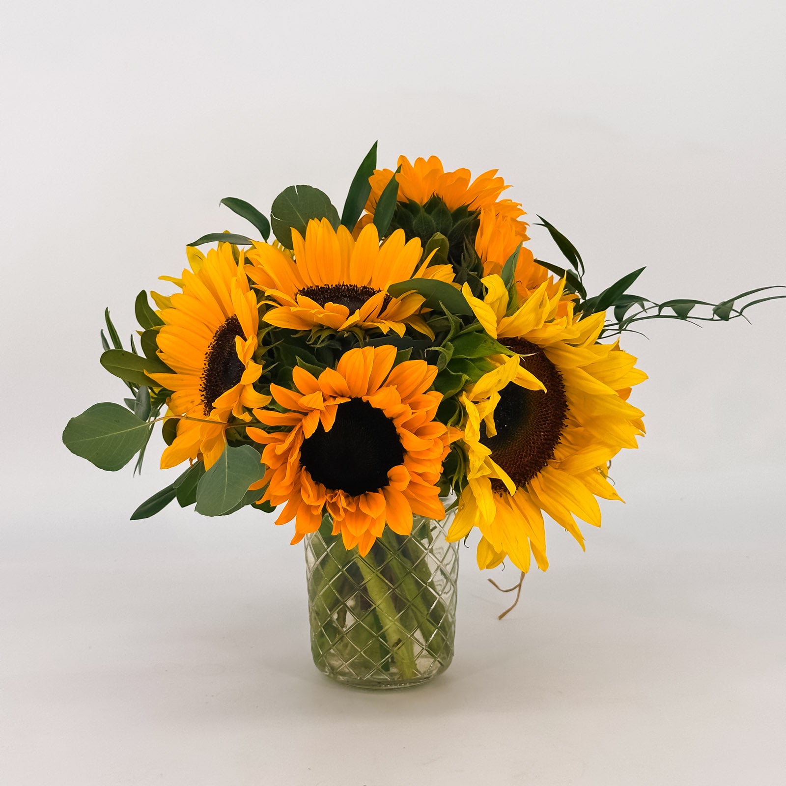 Summer Glow flower arrangement, a vibrant display of fresh sunflowers and eucalyptus in a clear glass vase, for premium Bay Area flower delivery.